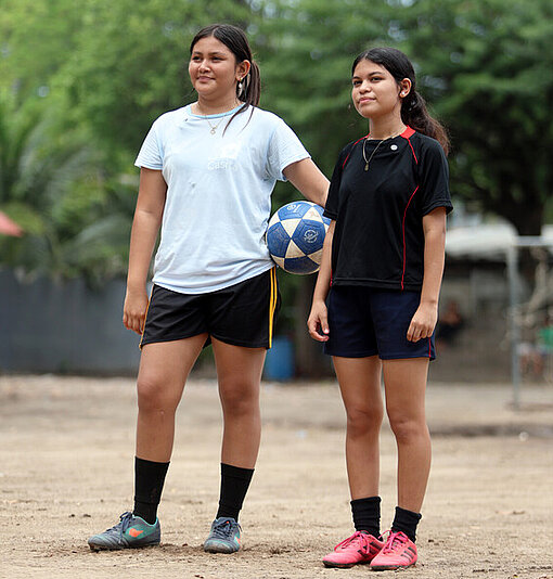 Viriginia und Saidia stehen draußen auf dem Fußballplatz ihrer Gemeinde