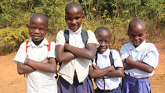 Vier afrikanische Kinder stehen nebeneinander mit verschränkten Armen und schauen verschmitzt in die Kamera.