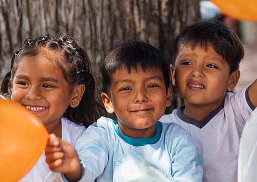 Drei kleine Kinder halten orange Luftballons