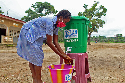 Ein Mädchen wäscht sich die Hände an einer neuen Hygienestation von Plan International