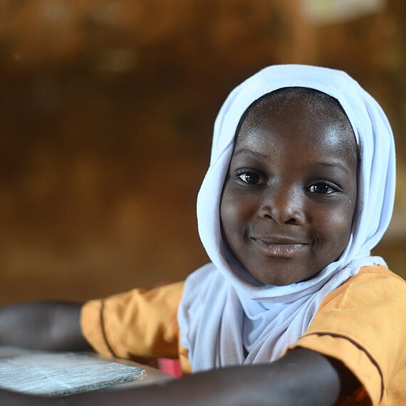 Ein kleines Mädchen sitzt an einem Tisch und lächelt in die Kamera