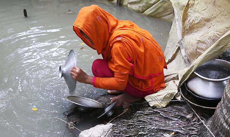 Ein Mädchen wäscht Geschirr in einer Wasserstelle
