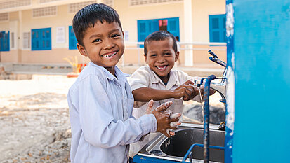 Zwei Jungs aus Kambodscha stehen an einer Handwasch-Station, die an ihrer Schule von Plan International gebaut wurde.
