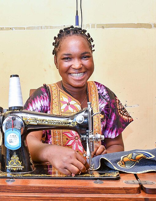 Ein junge Frau sitzt lächelnd an einer Nähmaschine