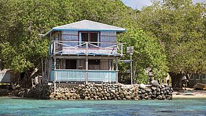 Ein einfaches Haus auf den Salomonen steht direkt am Wasser, geschützt durch eine Steinmauer – Symbol für die Folgen des Klimawandels.