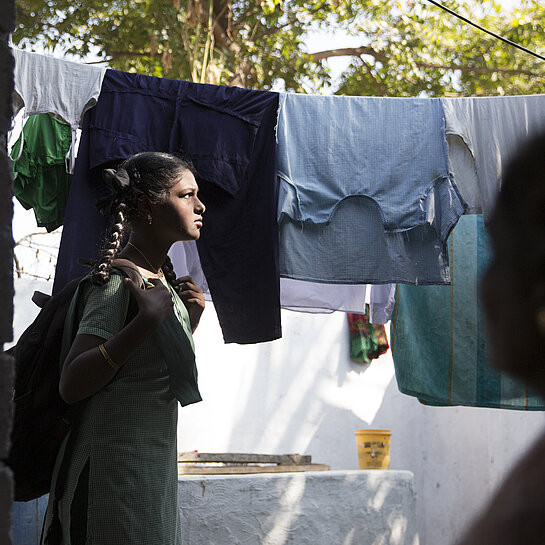 Mädchen steht im Sonnenlicht vor einer Wäscheleine.