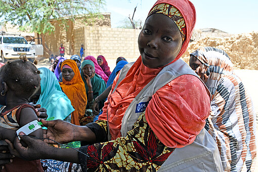 Eine Frau misst den Oberarmumfang eines kleinen Kindes