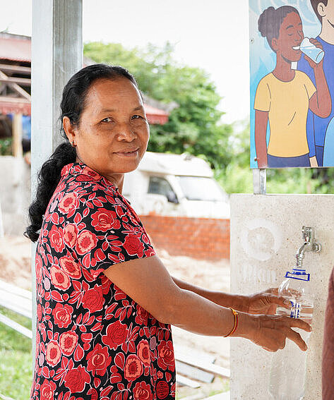 Eine Frau füllt an einem Wasserspender sauberes Trinkwasser in eine wiederverwendbare Wasserflasche.