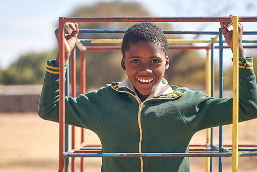 Kimberly hält sich an einem Klettergerüst fest und lächelt glücklich in die Kamera