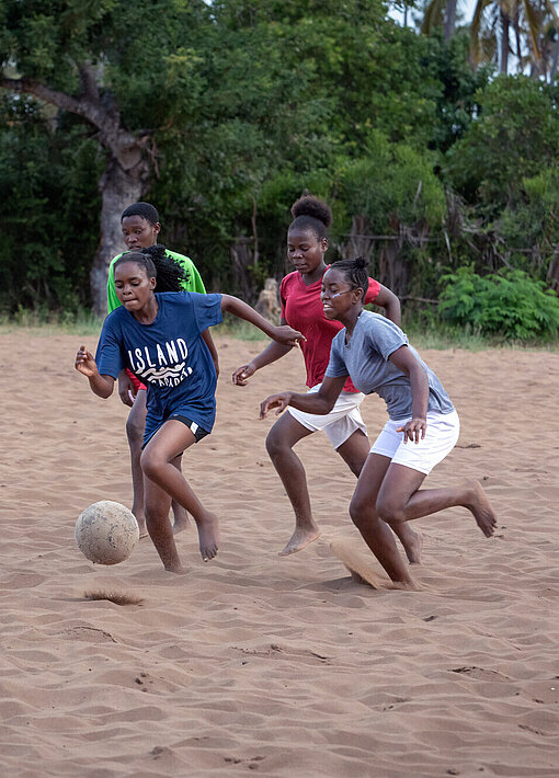 Vier Mädchen laufen durch den Sand und spielen Fußball