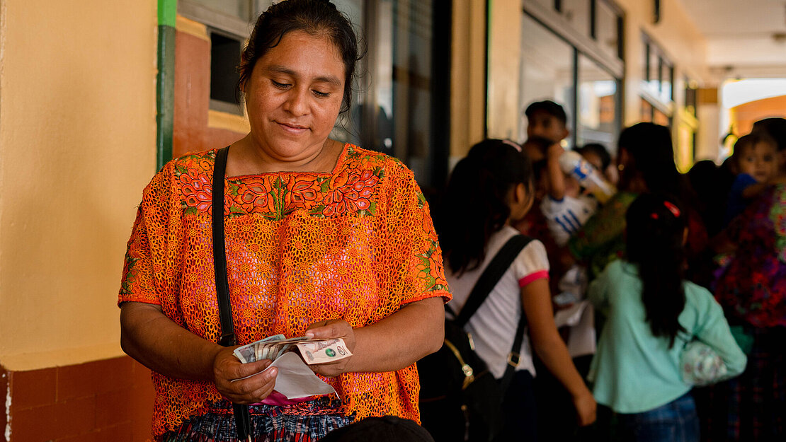 Eine Frau steht vor einem Gebäude und zählt Bargeld in ihrer Hand