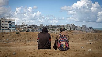 Ein Blick auf eine sandige Straße mit zerschossenen Häusern und zwei Männern