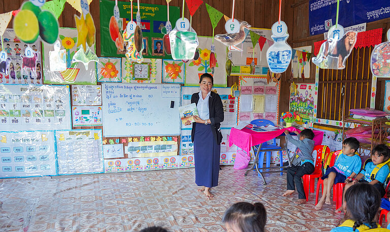 Vorschullehrerin vor ihren Schüler:innen im bunt eingerichteten Klassenraum