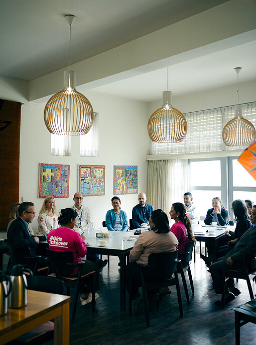 Mehrere Erwachsene und ein Mädchen sitzen an einem runden Tisch und unterhalten sich