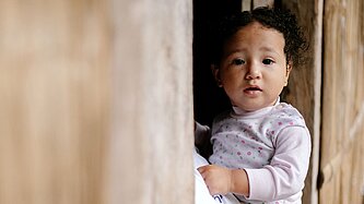 Mayras kleine Tochter blickt aus einem Fenster ihres Zuhauses in der ecuadorianischen Provinz Manabí.