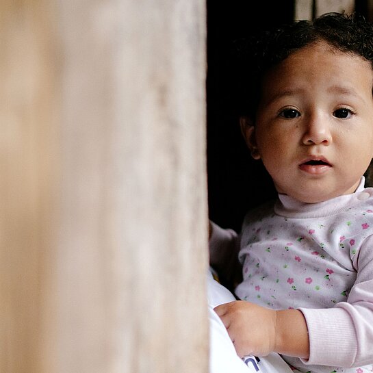 Mayras kleine Tochter blickt aus einem Fenster ihres Zuhauses in der ecuadorianischen Provinz Manabí.