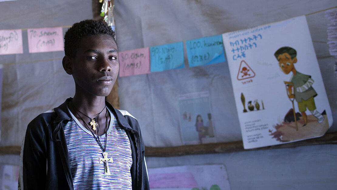 Ein Junge steht in einem Raum und schaut ernst in die Kamera.