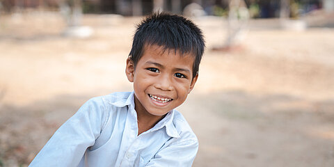Eine Junge aus Kambodscha lehnt sich nach rechts ins Bild. Er ist 9 Jahre alt und lacht Freude strahlend.