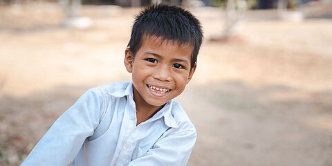 Eine Junge aus Kambodscha lehnt sich nach rechts ins Bild. Er ist 9 Jahre alt und lacht Freude strahlend.