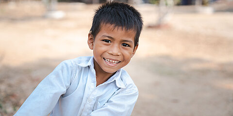 Eine Junge aus Kambodscha lehnt sich nach rechts ins Bild. Er ist 9 Jahre alt und lacht Freude strahlend.