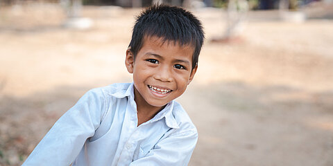 Eine Junge aus Kambodscha lehnt sich nach rechts ins Bild. Er ist 9 Jahre alt und lacht Freude strahlend.