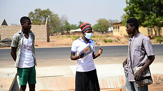 Eine junge Frau steht zwischen zwei jungen Männern und spricht mit ihnen