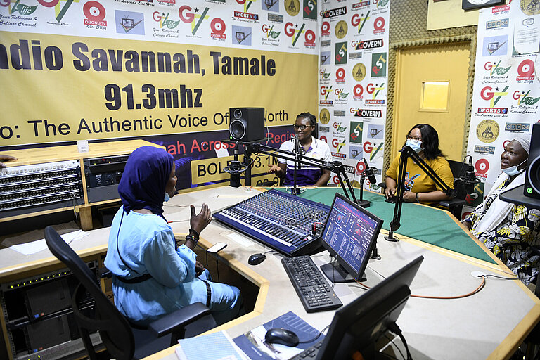 Eine Frau sitzt in einem Radiostudio und spricht mit drei weiteren Personen