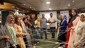Teilnehmende eines Workshops stehen im Kreis und halten ein Netz aus Schnüren – intergenerationeller Dialog mit Plan International in Ägypten.