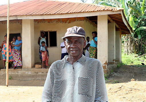 Der Dorfvorsteher steht vor der alten Schule und betont die Herausforderungen