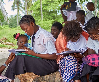 Schüler:innen sitzen auf einem Stein und schreiben