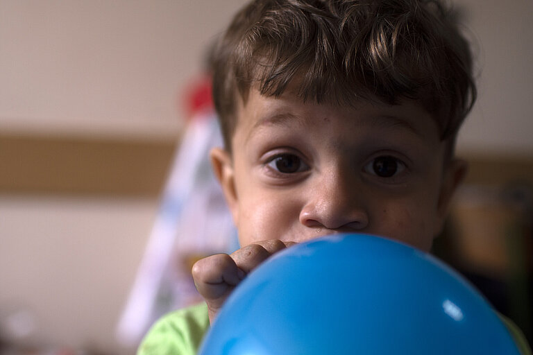 Ein Junge schaut in die Kamera und bläst einen Luftballon auf