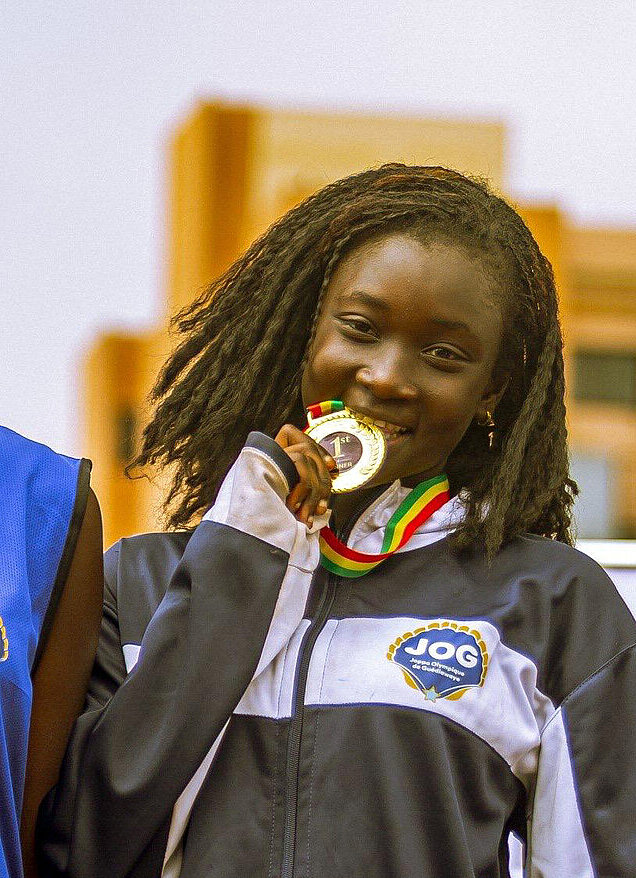 Drei junge Senegalesinnen stehen auf einem Podest, jede hat eine Medaille umhängen. Das Mädchen in der Mitte beißt auf ihre Medaille.