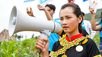 Ein Mädchen hält ein Megaphon und spricht hinein, hinter ihm stehen Jugendliche, die Schilder hochhalten