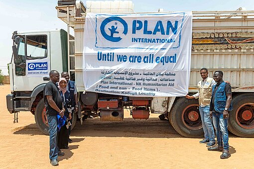 Mehrere Männer stehen zusammen vor einem Lastwagen mit der Aufschrift "Plan International - Until we are all equal"