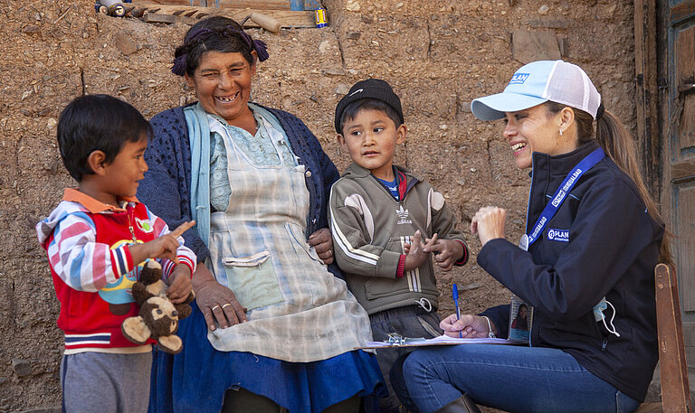 Zwei Jungen und ihre Großmutter sprechen mit einer Mitarbeiterin von Plan International.