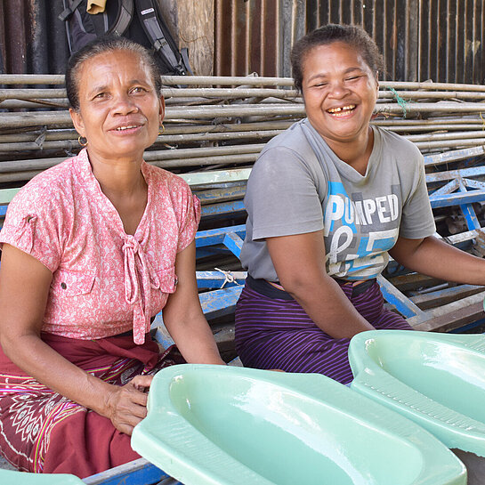 Zwei Frauen sitzen vor grünen Toilettendeckeln.