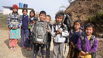 Grundschulkinder mit Rucksäcken lächeln in die Kamera. 