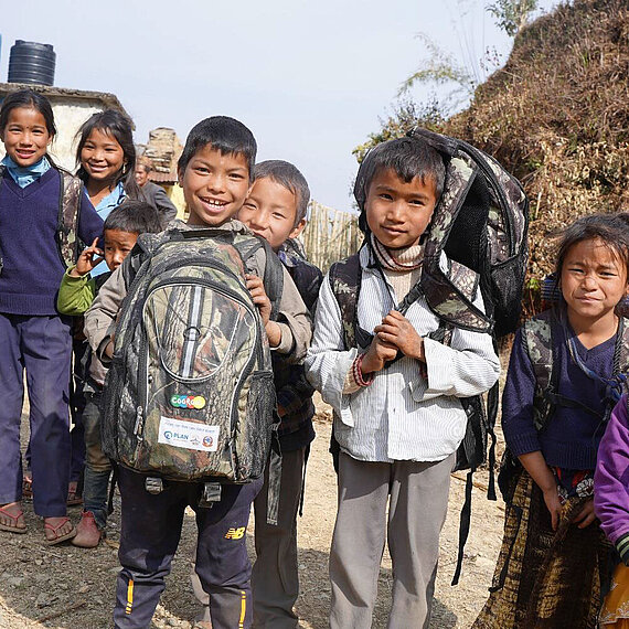 Grundschulkinder mit Rucksäcken lächeln in die Kamera. 