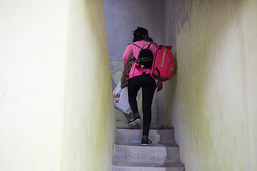 Eine junge Frau mit Rucksack und Tüte in der Hand läuft eine Treppe hoch