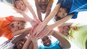  Mehrere Kinder bilden einen Kreis und legen lächelnd ihre Hände zur Mitte zusammen