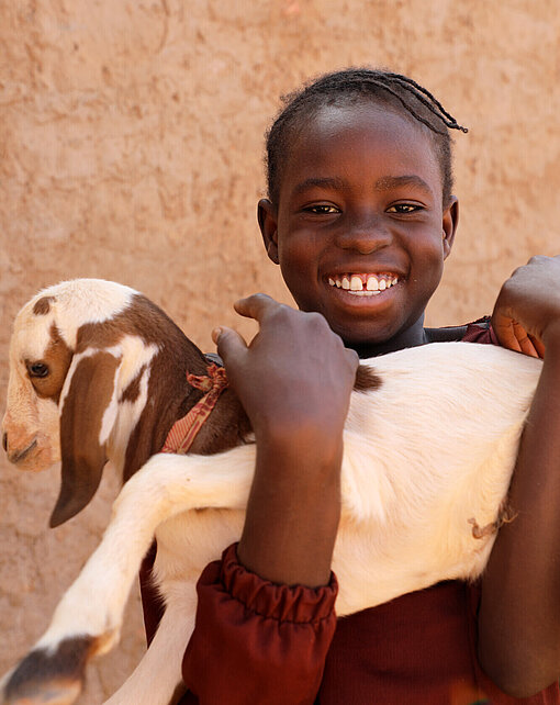 Ein Mädchen hält eine junge Ziege im Arm
