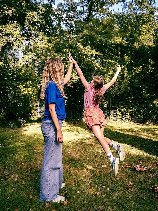 Ein Mädchen springt hoch und gibt einer Frau, die neben ihm steht, in der Luft ein High Five