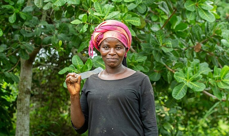 Frau vor Cashewfarm stehend