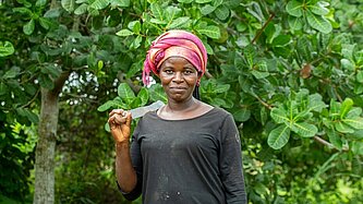 Frau vor Cashewfarm stehend