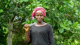 Frau vor Cashewfarm stehend