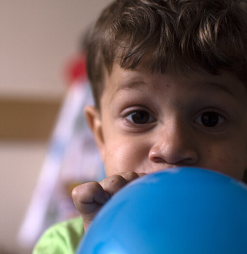 Ein Junge pustet einen blauen Luftballon auf