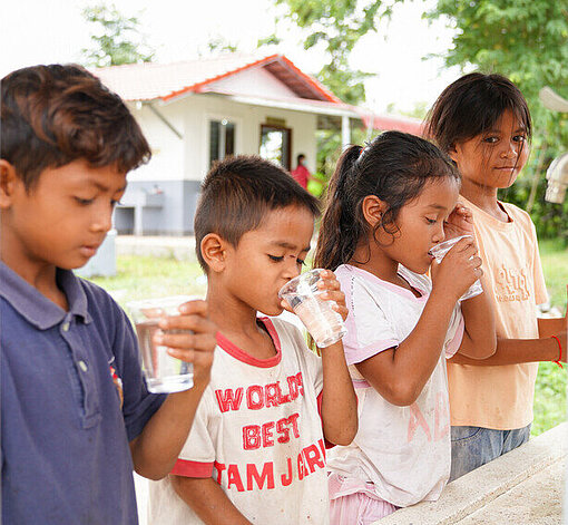Vier Kinder stehen gemeinsam an einem Wasserspender und trinken sauberes Wasser 