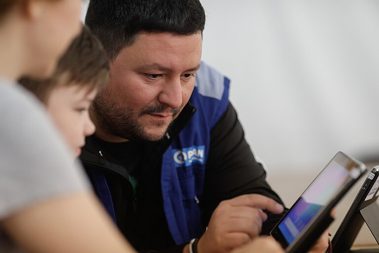 Ein Plan-Mitarbeiter unterstützt zwei Kinder beim Lernen am Tablet