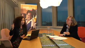 Online-Veranstaltung zur Bildungsförderung und Mädchenrechten im Rahmen von „Zukunft stiften mit Plan“. Zwei Frauen bei einer Online-Veranstaltung oder Besprechung in einem Konferenzraum. Im Hintergrund ein Roll-up mit dem Schriftzug „Zukunft stiften mit Plan“ und dem Bild eines Mädchens in Schuluniform.