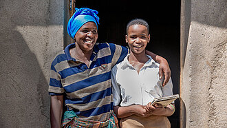 Proby und Ihre Mutter stehen Arm in Arm vor ihrem Haus in Ruanda